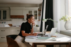 smiling-young-woman-making-notes-looking-laptop-while-working-home
