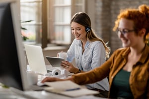 happy-female-entrepreneur-with-headset-drinking-coffee-while-surfing-net-touchpad-office